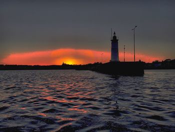 Lighthouse by sea against sky during sunset