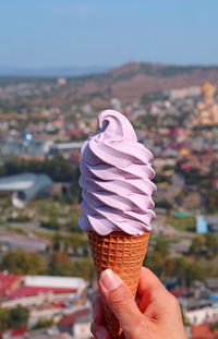 Woman's hand holding a georgian wine soft serve ice cream cone against blurry city view