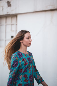 Young woman looking away while standing against wall