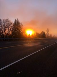 Road by trees against sky during sunset