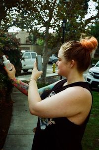 Woman photographing bottle while standing outdoors