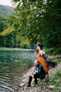 Woman sitting by lake against trees