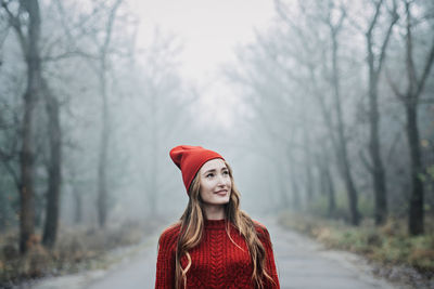 Woman in red hat and sweater walking on foggy mystical morning forest.