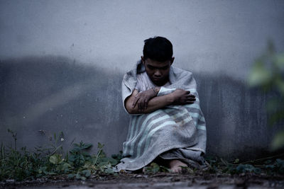 Full length of young man sitting against wall