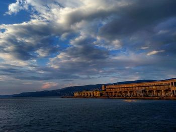 Sea by buildings against sky during sunset