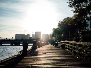 High angle view of boardwalk by river in city against sky on sunny day