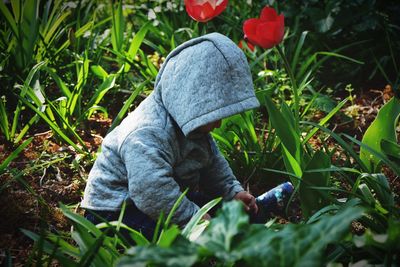 Baby girl in hooded jacket crouching on field