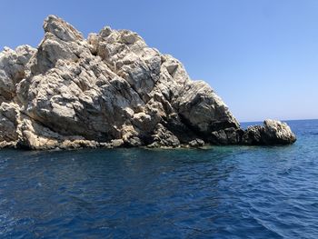 Rock formations in sea against clear blue sky