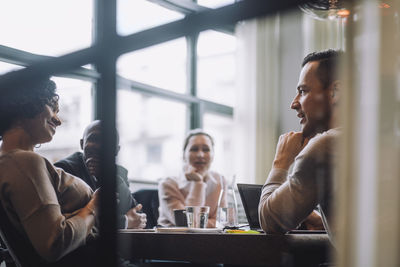 Mature businessman discussing plans with male and female colleagues sitting at conference table