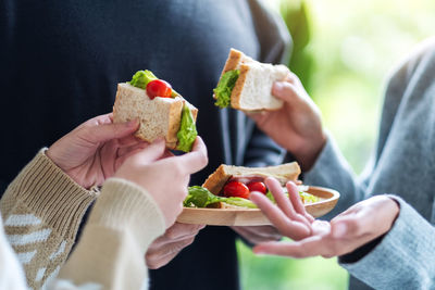 Group of young people holding and eating whole wheat sandwich in wooden plate together