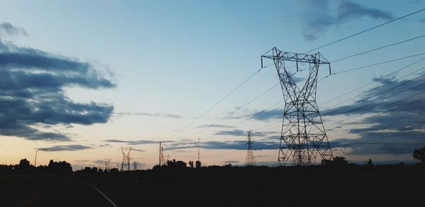 Low angle view of silhouette electricity pylons against sky at sunset