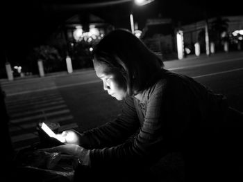 Woman using mobile phone while sitting on road at night