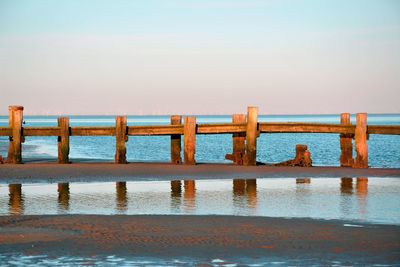 Wooden posts in sea against clear sky