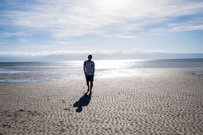 Full length of man walking at beach against sky during sunny day