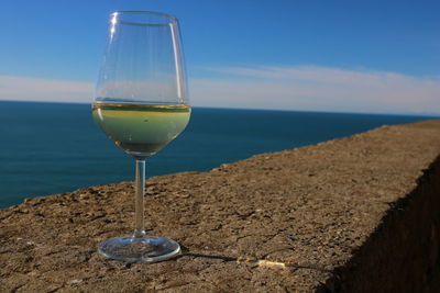 Close-up of wine glass on beach against sky