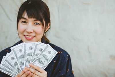 Close-up portrait of woman holding paper currency against wall