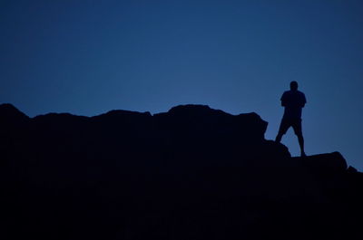 Low angle view of silhouette man standing on mountain against clear sky