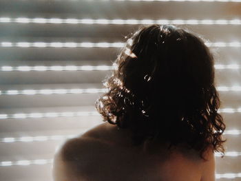 Close-up of shirtless woman against window blinds