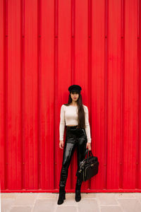 Portrait of young woman standing against red wall