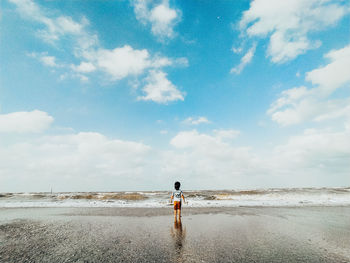 Rear view of person standing on beach against sky