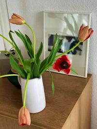 Close-up of hand holding red roses in vase at home