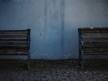 Cropped image of empty wooden benches on paving stone sidewalk against wall