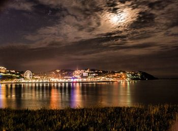 Illuminated city at waterfront during sunset