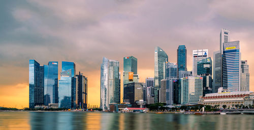 Sea by modern buildings against sky during sunset