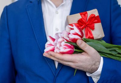 Man holding one tulip flower in hand or in jacket on palm.male in office suit with gift box, bouquet