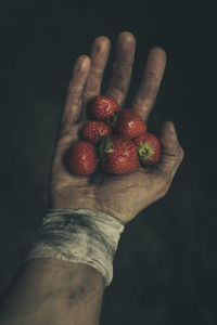 Close-up of hand holding strawberry over black background