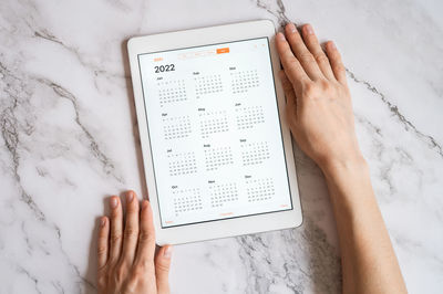 Tablet computer with an open app of calendar for 2022 year in a womans hands on a gray