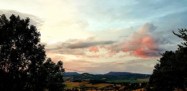 Silhouette trees by mountains against sky during sunset