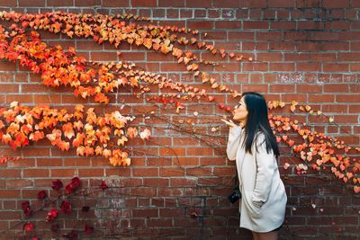 Side view of woman against wall blowing kiss to autumn leaves