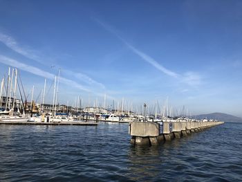 Sailboats moored at harbor against blue sky