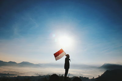 Man holding flag while standing on mountain against sky