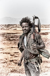 Portrait of man holding camera at beach against sky