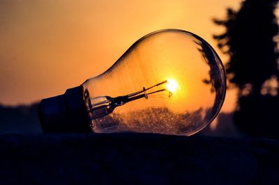 Close-up of illuminated light bulb against sky at sunset