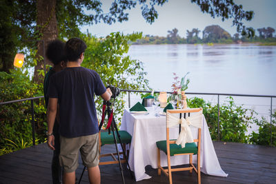 Rear view of people using camera while standing on deck