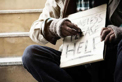 Midsection of man writing on cardboard while sitting on steps