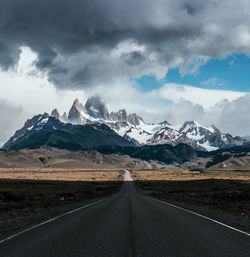 Road leading towards snowcapped mountains against sky