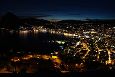 High angle view of illuminated city by sea against sky at night