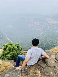 Rear view of man sitting on mountain - man sitting on the edge of a mountain
