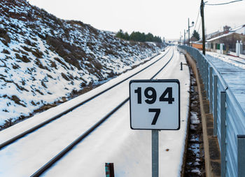 Road sign by snow covered railroad tracks against sky