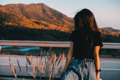 Rear view of woman standing by railing against mountain