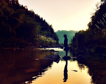 Silhouette man standing by lake against sky during sunset