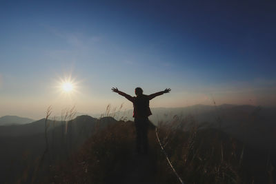 Man with arms outstretched standing on mountain against sky during sunset