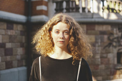 Portrait of young female student with brown hair standing outside university