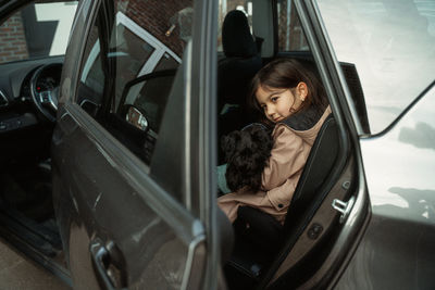 Portrait of young girl sitting  in car holding a dog