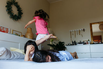 Two children lying on the bed and other child jumping over