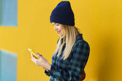 Young woman using mobile phone against yellow wall